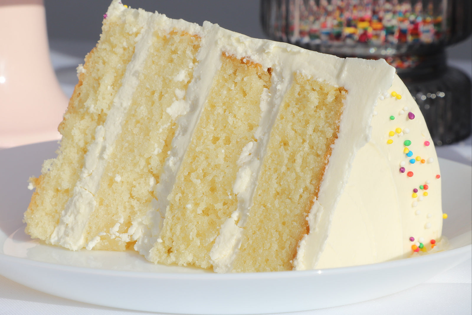 Slice of layered cake on a white plate with a pink cake stand in the background.
